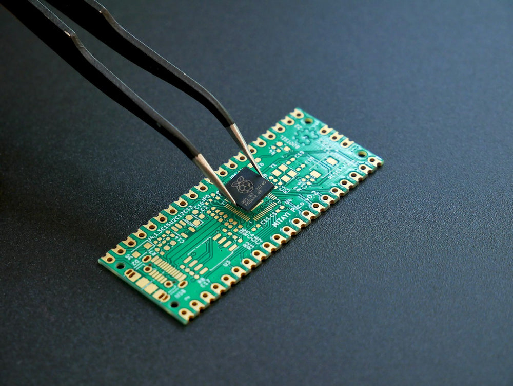 Tweezers placing a small chip on a green circuit board
