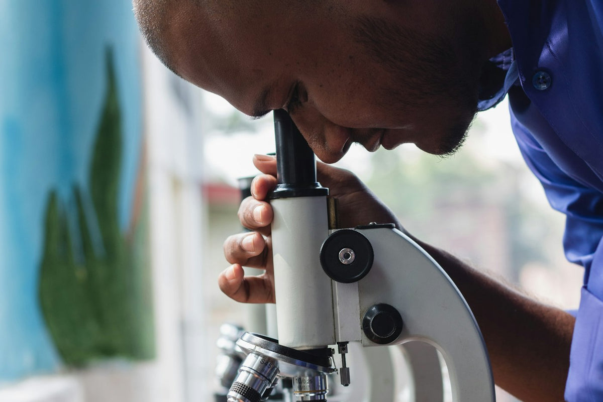 A man leaning over a microscope by a window at home