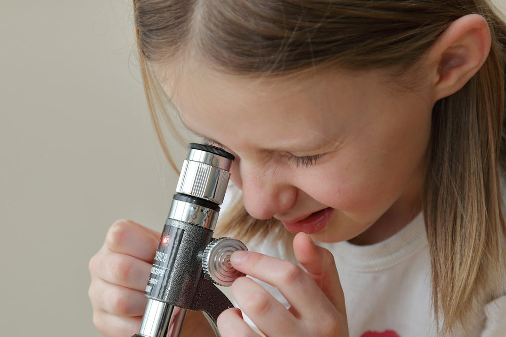 A young girl smiling as she looks into a microscope at home