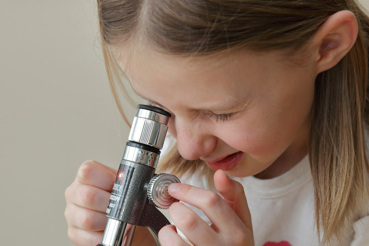 A young girl smiling as she looks into a microscope at home